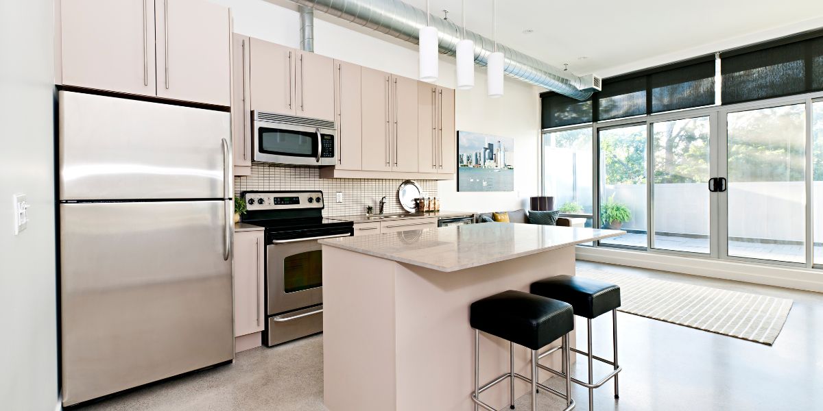 Modern kitchen with stainless steel appliances and a large island, featuring bright natural lighting.