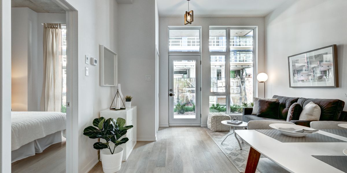 Contemporary living room with large windows, light-colored decor, and a view of an adjacent bedroom.