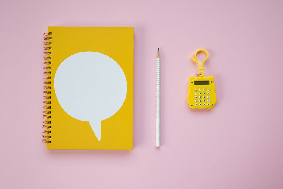 A minimal flat lay on a bright surface showing a calculator, a notebook, a pen, and house keys, representing financial planning for a home sale.