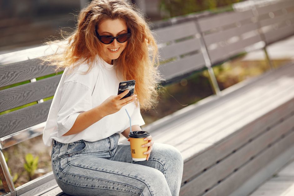 A woman stands outside a clean, modern storefront, smiling as she looks at her phone, illustrating a positive customer experience finding a local business.